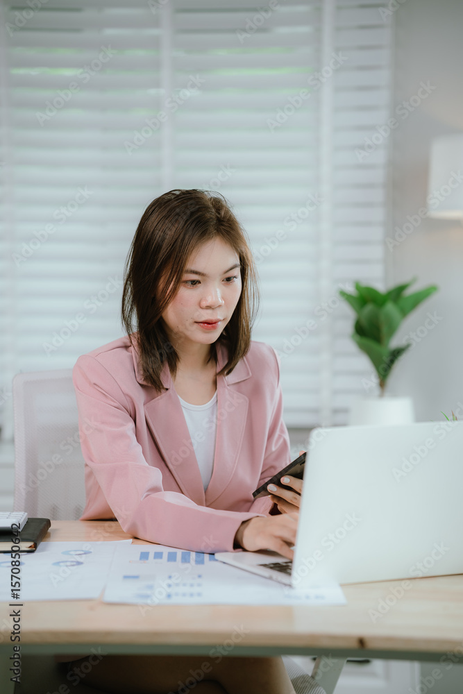 Businesswoman in pink coat working at desk using smartphone and laptop, managing tasks and planning projects in modern and organized office environment. Businesswoman in pink coat working at desk using smartphone and laptop, managing tasks and planning projects in modern and organized office environment.