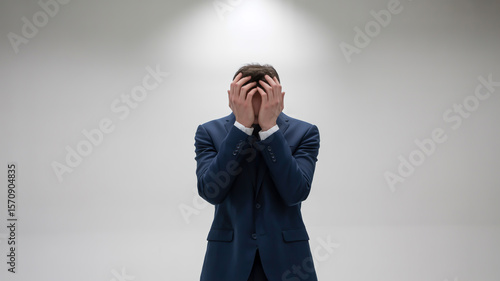 A back view photograph of a person in a dark navy business suit with white dress shirt, standing against a plain white background.