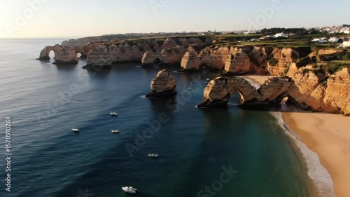 Golden sunlight bathes the sandstone cliffs and arches along the algarve coast, as boats dot the azure sea near marinha beach