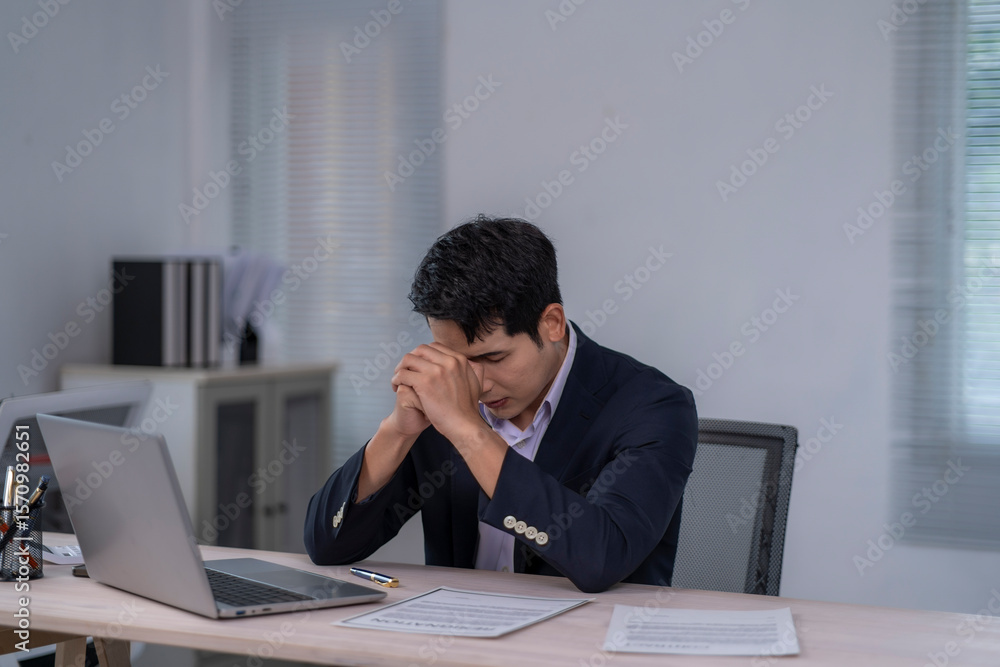 A man is sitting at a desk with a laptop and a stack of papers A man is sitting at a desk with a laptop and a stack of papers