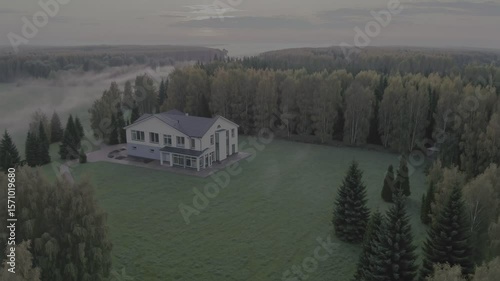 Drone photo of modern countryside house surrounded by forest and misty sunrise ideal for real estate rural living and autumn stock themes. Aerial view of country house at sunrise

