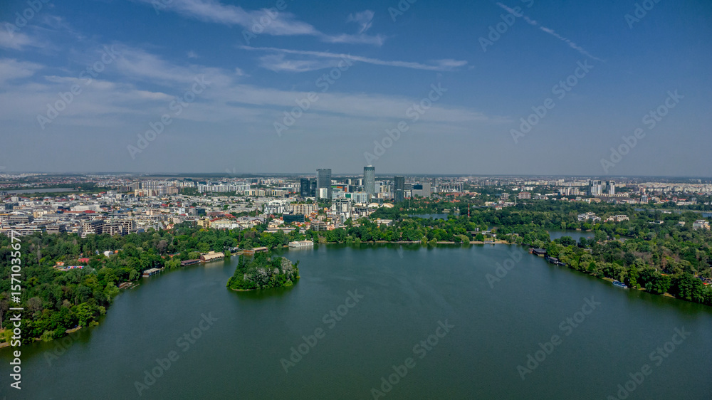 Naklejka premium Wide drone shot of Herastrau Lake with city skyline, modern office buildings, and lush urban forest