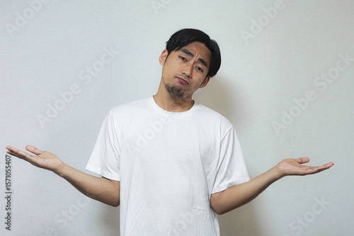 A young man in a white t-shirt shrugs, expressing uncertainty or indifference.