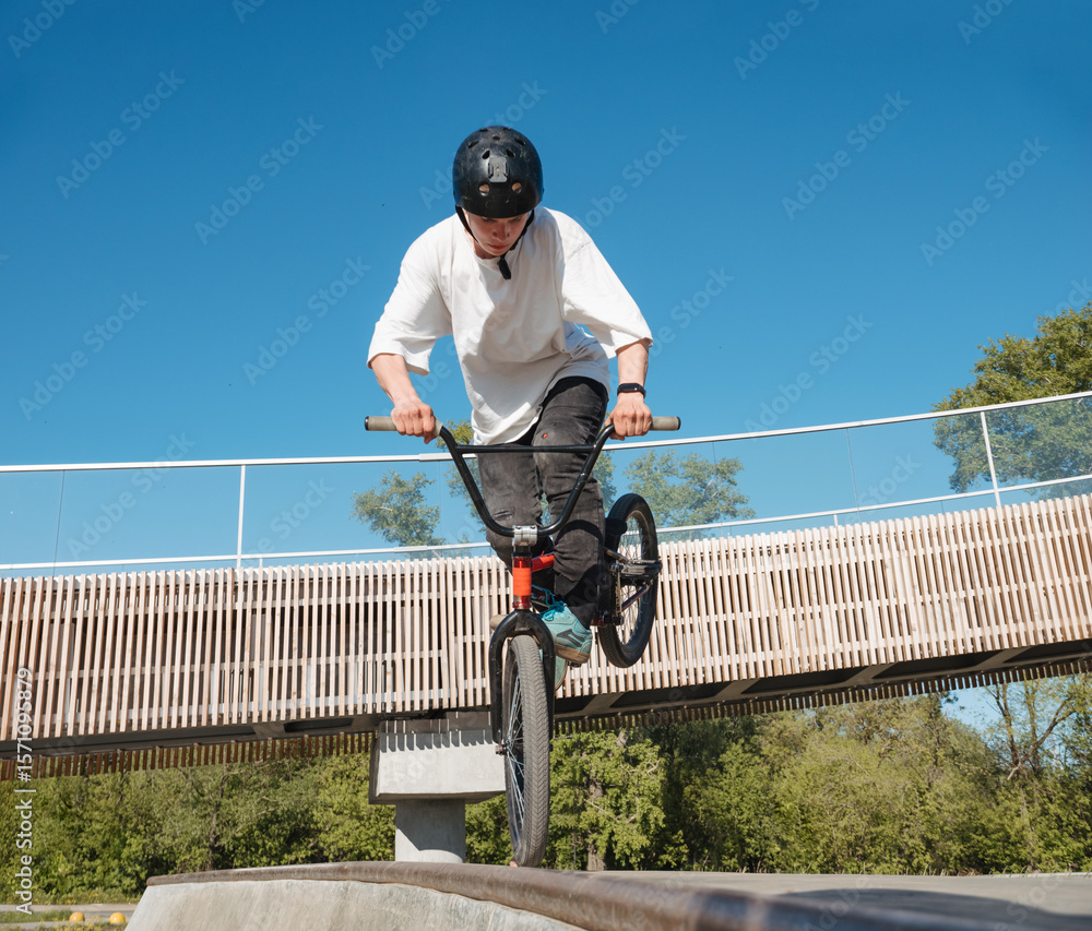 Naklejka premium Skilled BMX rider performing Footjam trick in ramp park. Young BMX bicycle rider having fun and posing in Footjam outdoors. Footjam trick is front wheel stand. Concrete ramp street park