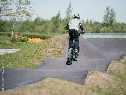 Child on bmx bike on pump track. Young male cyclist in helmet and protection rides bmx bike on asphalted bicycle race track. Boy BMX rider having fun and training on racing speed track. Extreme sport