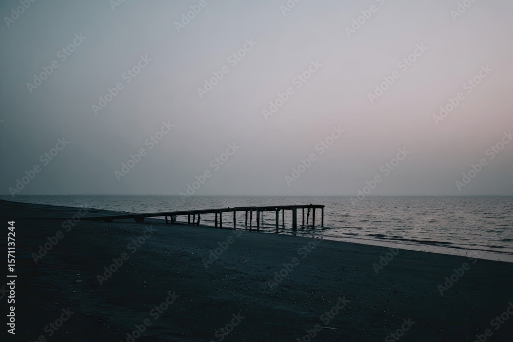 Fototapeta premium Misty beach scene with a weathered pier