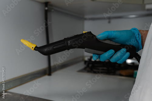 Wallpaper Mural Professional cleaning specialist wearing blue protective gloves holding steam cleaner, preparing to sanitizing gas stove surface for thorough kitchen hygiene, close-up. Concept of cleaning, household. Torontodigital.ca