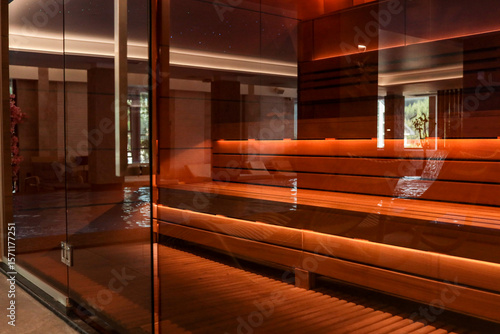 Quadro su tela Modern wooden sauna with warm lighting behind a glass wall, located near an indo