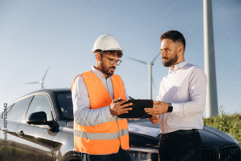 Naklejka premium Instructions for guy in hard hat. Two men engineers are on field, with wind turbines