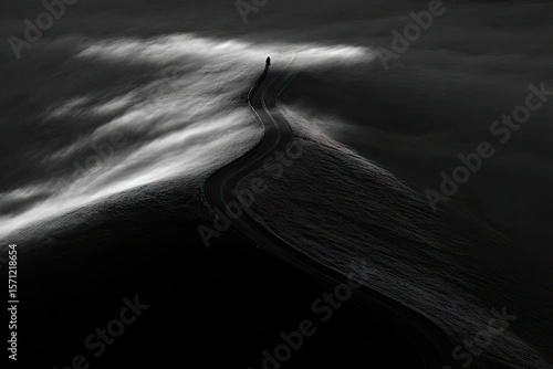 A winding road, seemingly lost in a sea of mist, leads into a dark, ethereal landscape. A solitary figure traverses the road