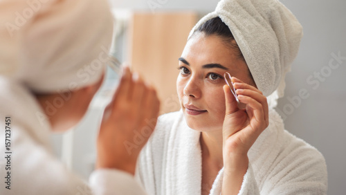 A beautiful young woman plucking her eyebrows in the mirrror