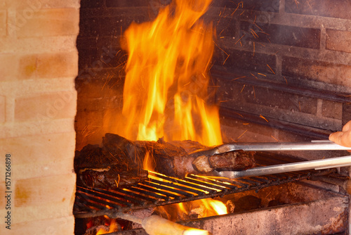 Sizzling Steaks Grilling Over Open Flames in a Brick BBQ
Thick cuts of meat sizzle on a grill over roaring flames within a brick barbecue, with tongs turning one of the steaks