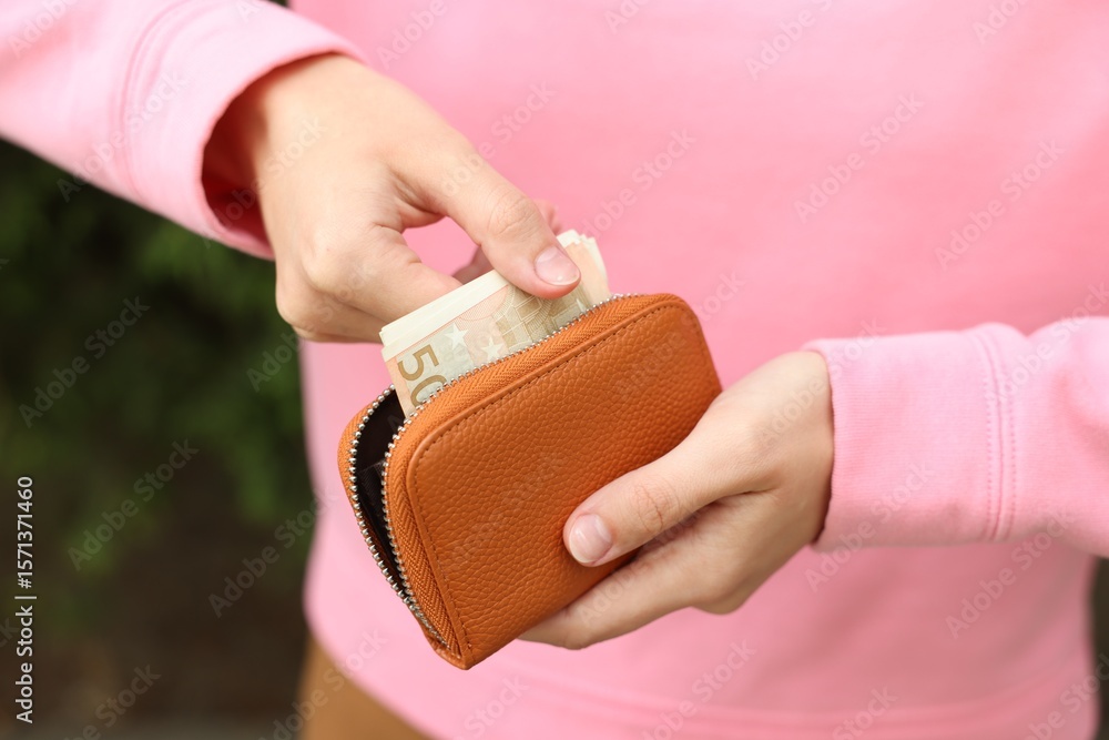 Obraz premium Woman putting money into wallet outdoors, closeup
