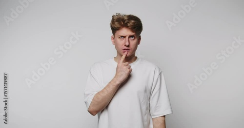 Young man pondering with curious expression in a minimal studio setting, capturing a moment of thought