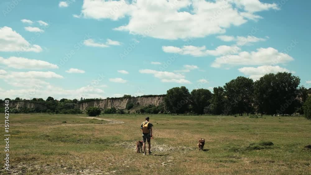 Man walking with two dogs German and Australian Shepherd across a wide grassy plain with dramatic cliffs in the distance. Travel with pets concept. Natural oasis Belegis - Serbia country Man walking with two dogs German and Australian Shepherd across a wide grassy plain with dramatic cliffs in the distance. Travel with pets concept. Natural oasis Belegis - Serbia country