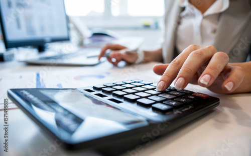 Businesswoman using calculator for financial accounting in modern office.