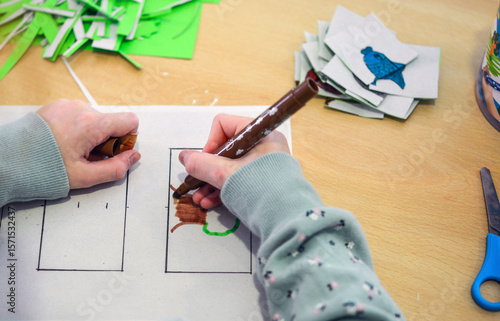 Konzept Kunst und Kreativität Kinder: Blick auf einen Tisch, wo ein Mädchen bunte Bilder ausmalt und dann ausschneidet.