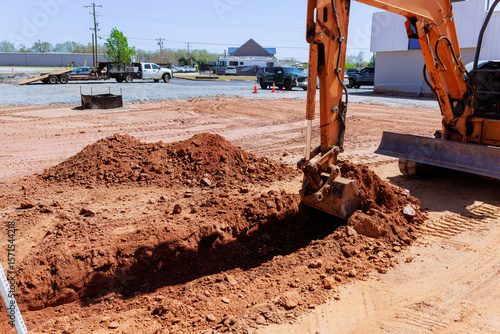 Fotografija Excavator works on construction site creating trench while trucks are parked nea