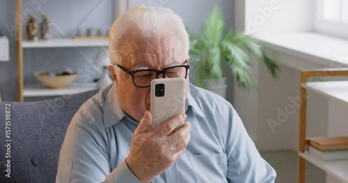 Elderly man has bad eyesight, puts off eyeglasses and focused in smartphone screen, tries to read received message, cannot understand how to use app, has some problems. Technology annd retirement