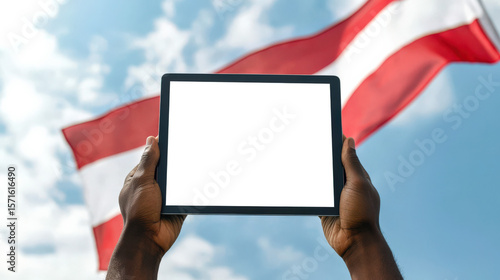 A mockup of a black tablet with an empty white ekar in the hands of a black guy, close-up. Celebration of the Independence Day of Austria. The red-white-red flag of Austria is flying in the sky