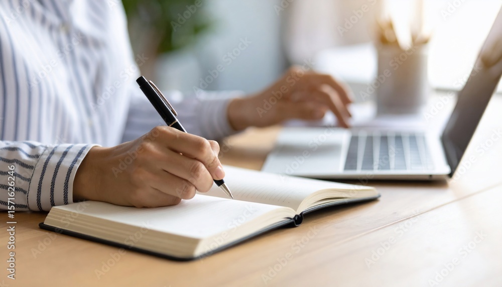 Woman writing in a notebook while using a laptop, working at a desk in a bright office. Woman writing in a notebook while using a laptop, working at a desk in a bright office.