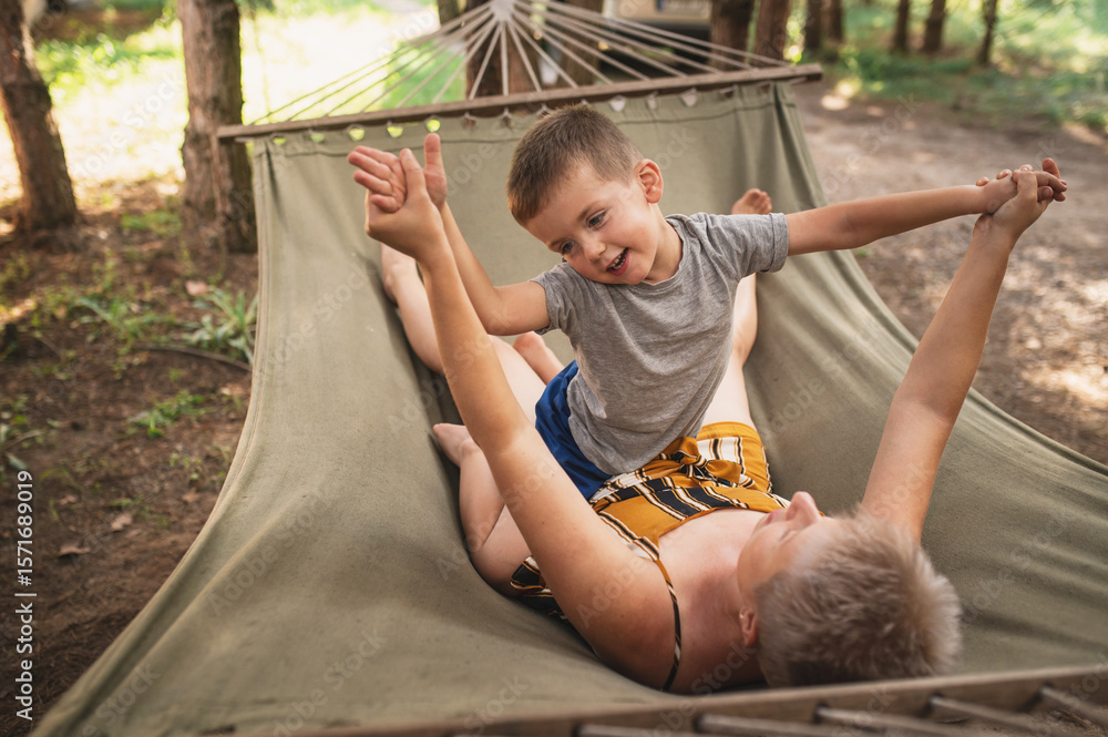Obraz premium Emotional Mother and son are fooling around in a hammock in the summer forest. Family outdoor recreation, hugs, emotions. Time spent together