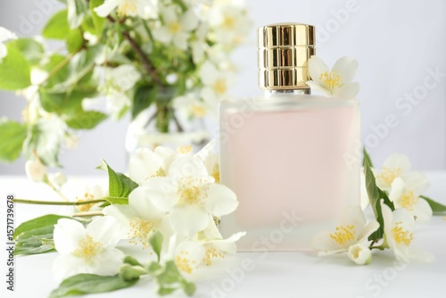 Bottle of perfume and jasmine flowers on white table, closeup