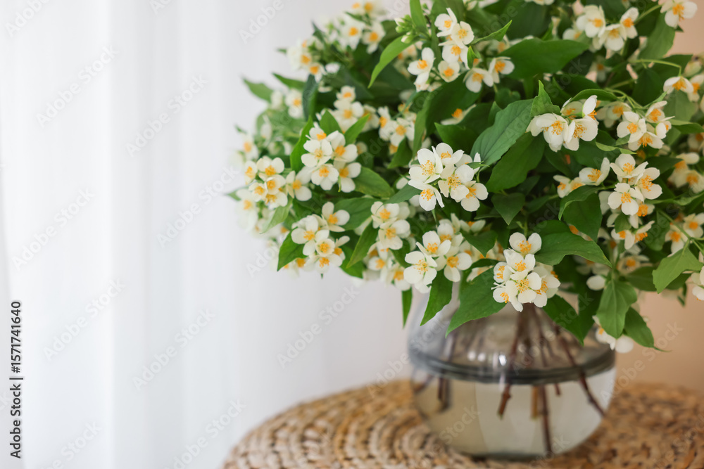 Beautiful jasmine flowers in vase on wicker table near window indoors, closeup. Space for text Beautiful jasmine flowers in vase on wicker table near window indoors, closeup. Space for text