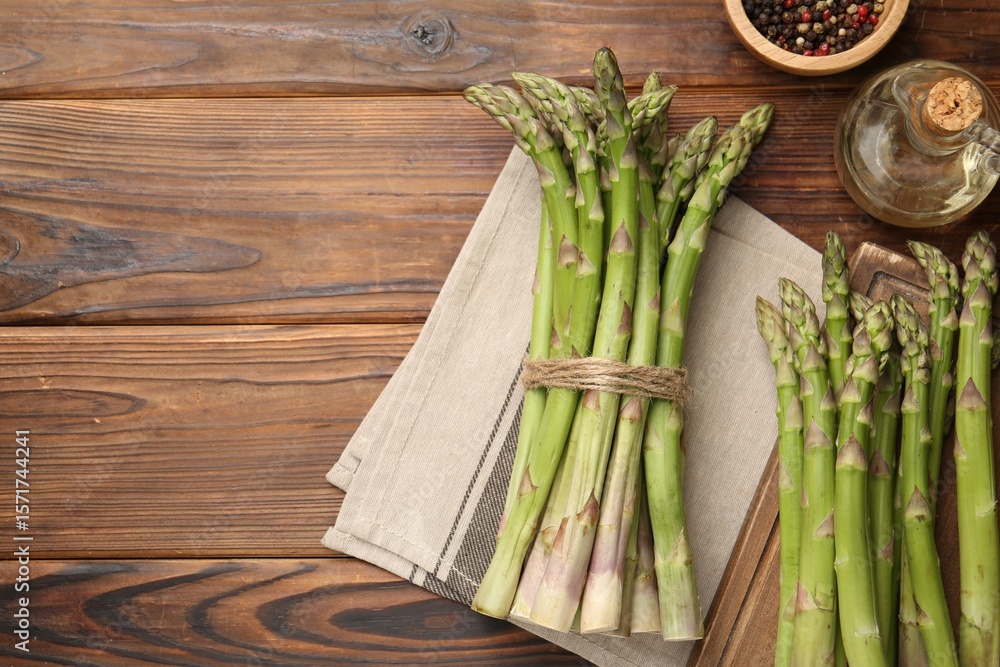 Fresh raw asparagus, spices and oil on wooden table, flat lay. Space for text Fresh raw asparagus, spices and oil on wooden table, flat lay. Space for text