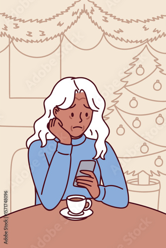 Dark skinned elderly woman sits alone with hot tea mug indoors on Christmas night, feeling lonely and thoughtful while surrounded by warm lights