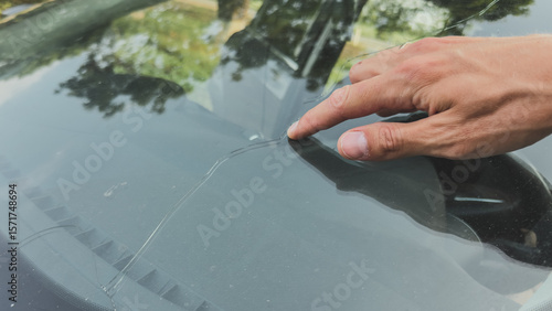 Close-up of a hand pointing at a long crack in a car windshield, highlighting glass damage and need for repair or replacement, vehicle maintenance concept