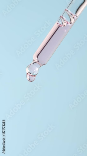 A transparent pink drop falls from a pipette on a light blue background. Perfect for beauty, cosmetic, and skincare vertical content.