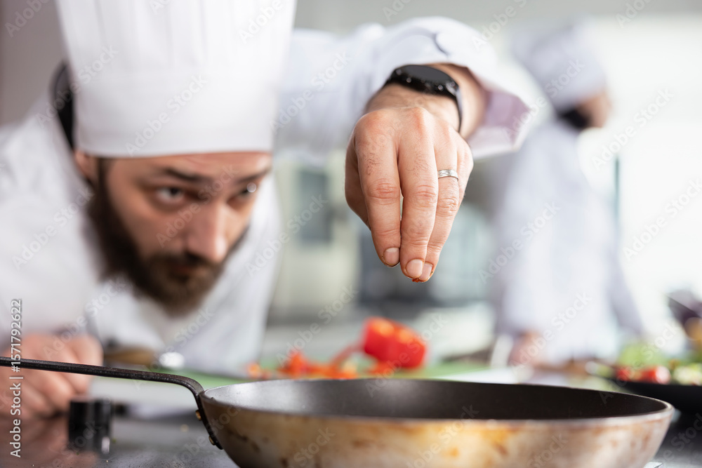 Focused male cook garnishing a dish with freshly cut vegetables on the stove, ensuring each plate meets gourmet and fine dining standards. Young head chef sprinkling bell pepper slices. Focused male cook garnishing a dish with freshly cut vegetables on the stove, ensuring each plate meets gourmet and fine dining standards. Young head chef sprinkling bell pepper slices.