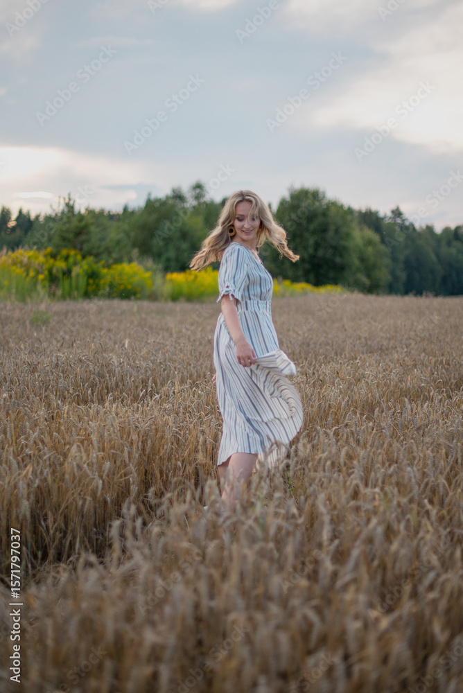 A stylish young woman in a summer dress poses in front of a golden wheat field. Fashion, glamour, and lifestyle concepts. A stylish young woman in a summer dress poses in front of a golden wheat field. Fashion, glamour, and lifestyle concepts.