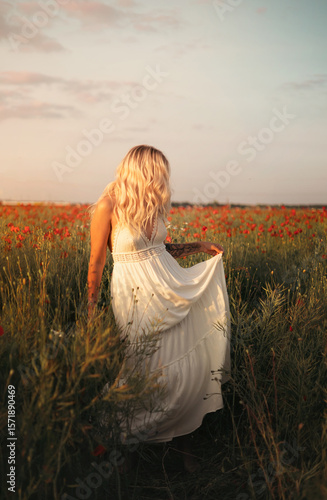young beautiful blonde woman in white dress in poppy field at sunset. Woman and nature