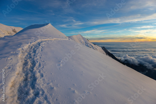 Mont Blanc ascent views on snow-covered ridge, surrounded by alpine peaks under clear and cloudy sky. High-altitude mountaineering, glacier terrain, mountain landscape outdoor expedition in Alps