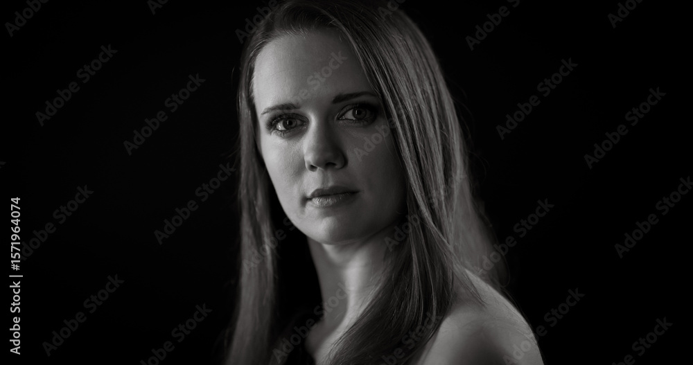 Fototapeta premium Black and white portrait of a serious young Caucasian woman with long hair posing in the studio
