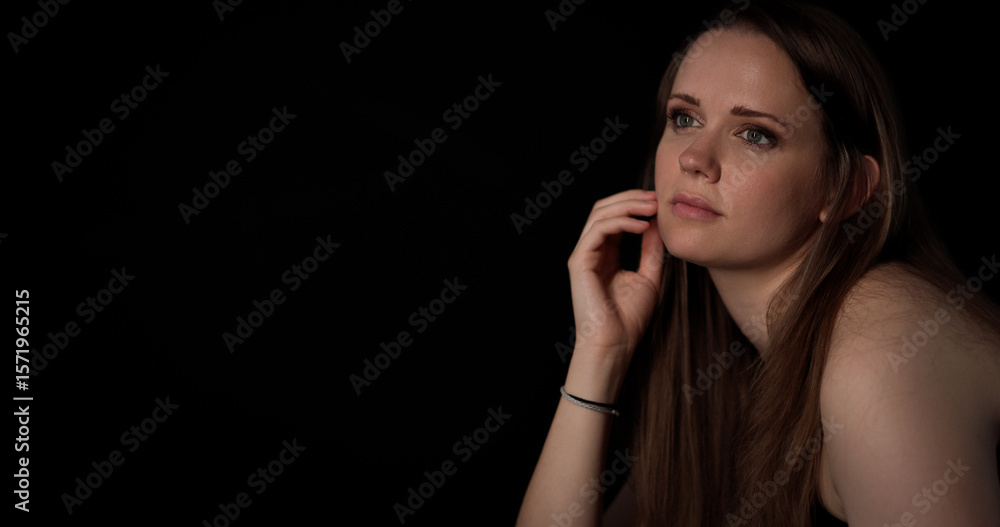 Fototapeta premium Thoughtful young woman with hand on face looking away against black background