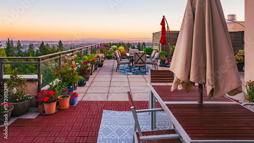 Sunset on large BC rooftop penthouse patio with deck furniture and umbrellas, with view across valley to Gulf Islands on far horizon.