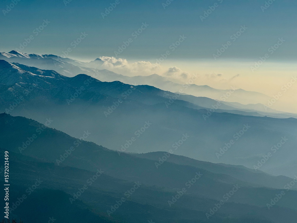 Obraz premium Hazy blue mountain layers fading into the distance. Scenic landscape with snow-capped peaks and atmospheric haze. Serene nature background.