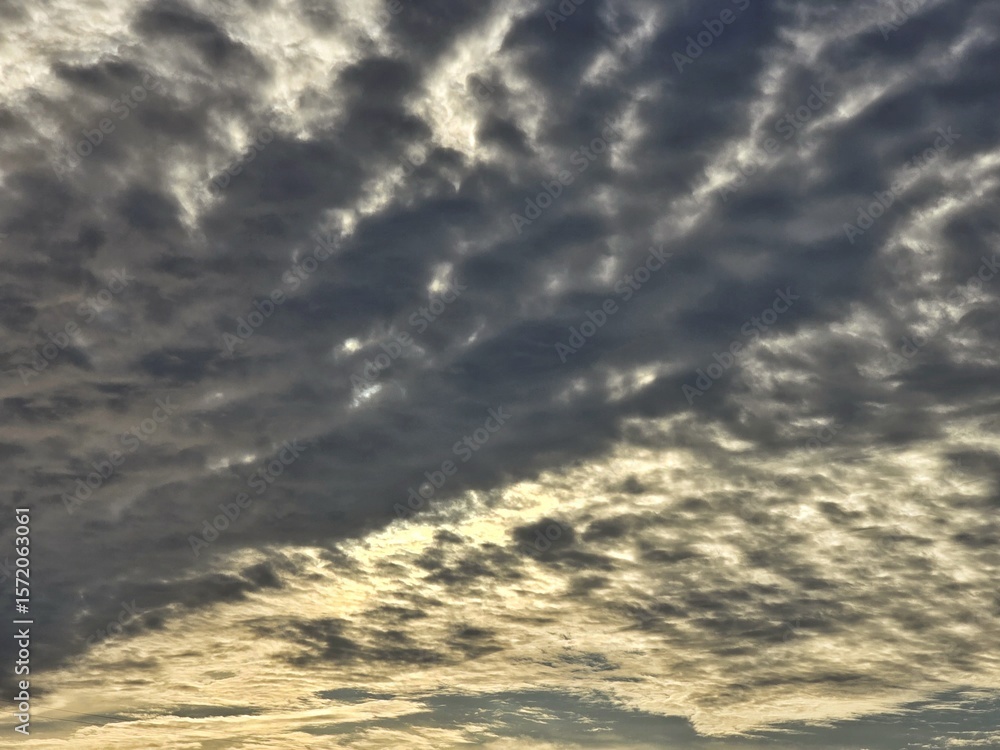Fototapeta premium Dramatic sunset sky with layered clouds and soft golden light breaking through. A natural cloudscape background with a moody and atmospheric feel, perfect for creative or editorial use.
