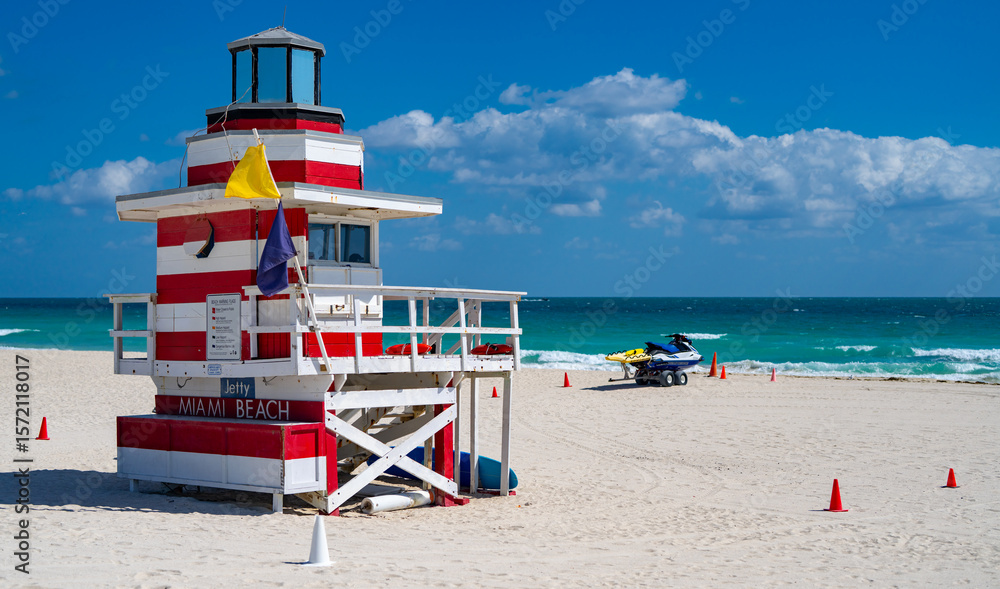 Fototapeta premium Miami Beach lifeguard at the summer beach. Tourism on South Miami Beach. Sky above lifeguard tower in Miami. Iconic lifeguard tower on sand in Miami. A symbol of Miamis coast.