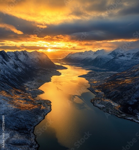 Golden Sunlight bathes a fjord, reflecting on water between snow-capped mountains in Norway.