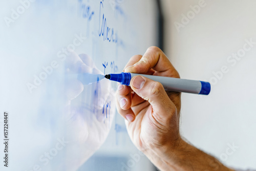 A hand writing on a whiteboard with a blue marker in a close up shot view
