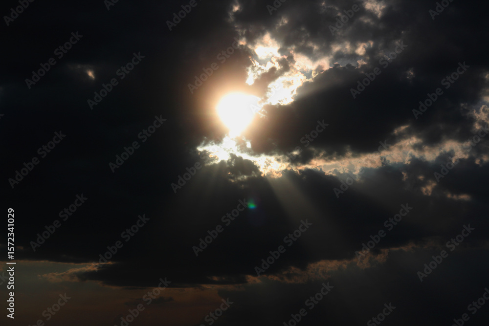 Fototapeta premium Sunlight breaking through dark clouds in a dramatic sky during late afternoon hours