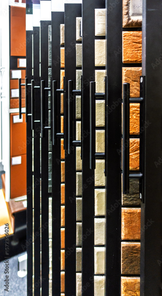 Obraz premium Close-up of wall tile samples displayed on a rack in a showroom, showing various textures and colors like orange and beige. Modern interior design concept.