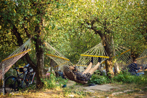 Wallpaper Mural People relaxing in hammocks in a green outdoor park or garden, enjoying leisure time and summer nature. Bicycles are parked nearby, suggesting outdoor activity. Torontodigital.ca