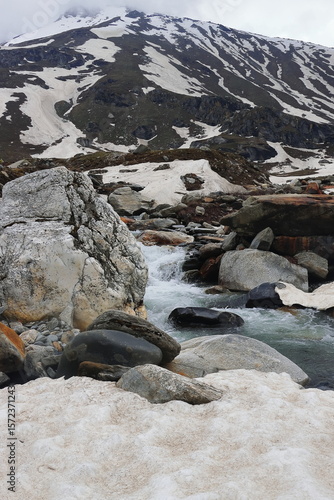 mountain stream flowing through the snow covered alpine valley at marhi near rohtang pass, himalaya mountains at manali in himachal pradesh, india