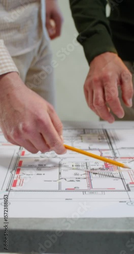 Two men are discussing a house construction project. They are talking standing next to a table in an unadorned room