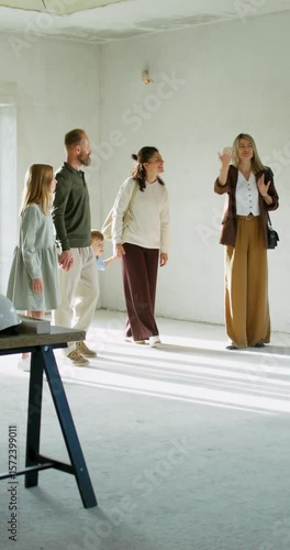 The realtor shows the house to a family with children. They walk around the room without decoration